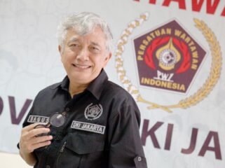 Foto: Seorang pengurus Persatuan Wartawan Indonesia (PWI) DKI Jakarta berpose di sela kegiatan organisasi, dengan latar belakang logo PWI