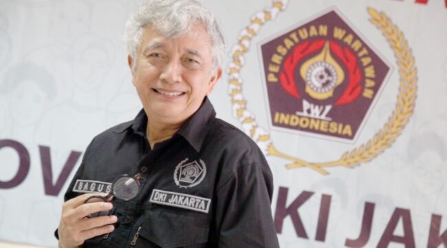 Foto: Seorang pengurus Persatuan Wartawan Indonesia (PWI) DKI Jakarta berpose di sela kegiatan organisasi, dengan latar belakang logo PWI